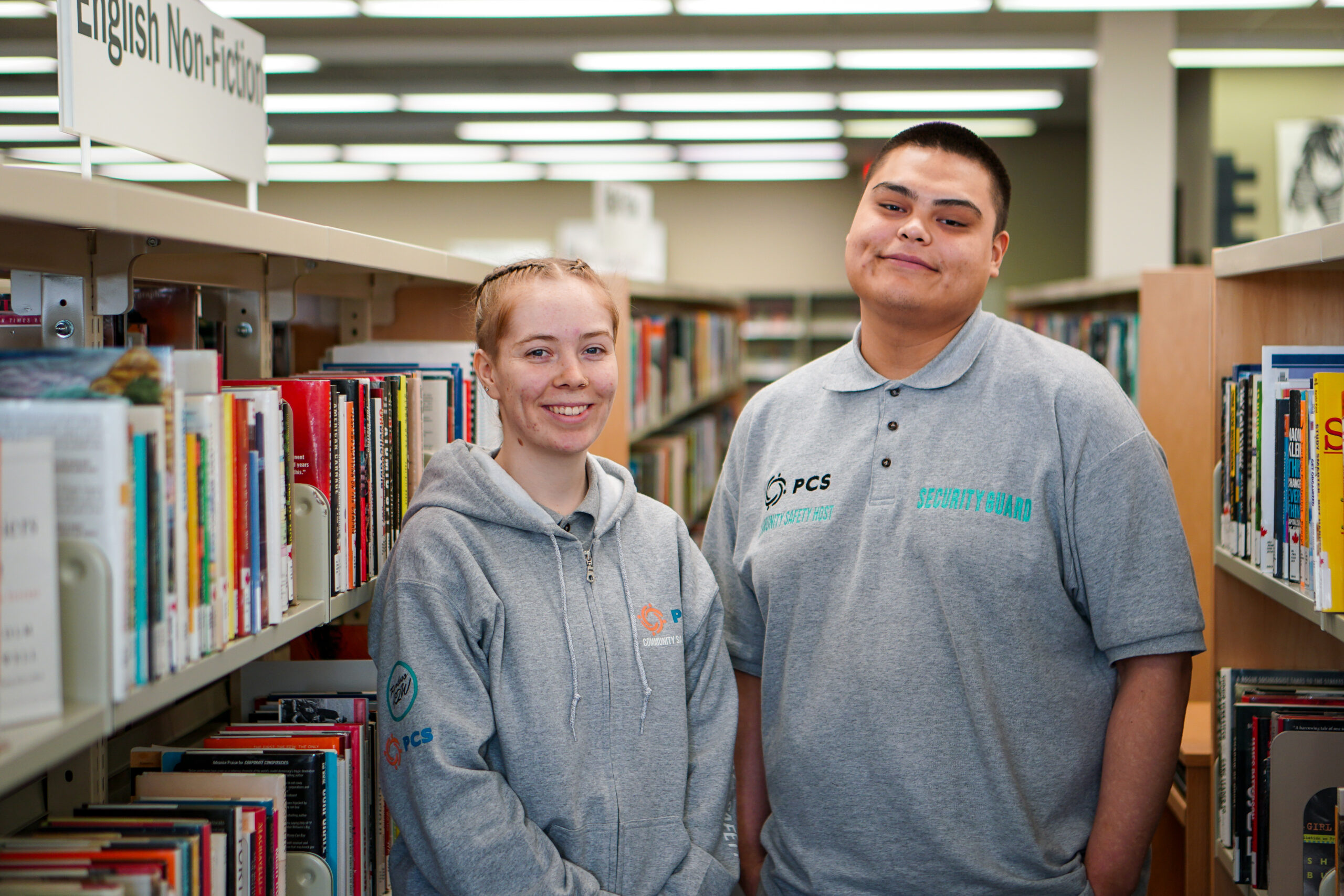 Two Community Safety Hosts posing together in library's non-fiction section.